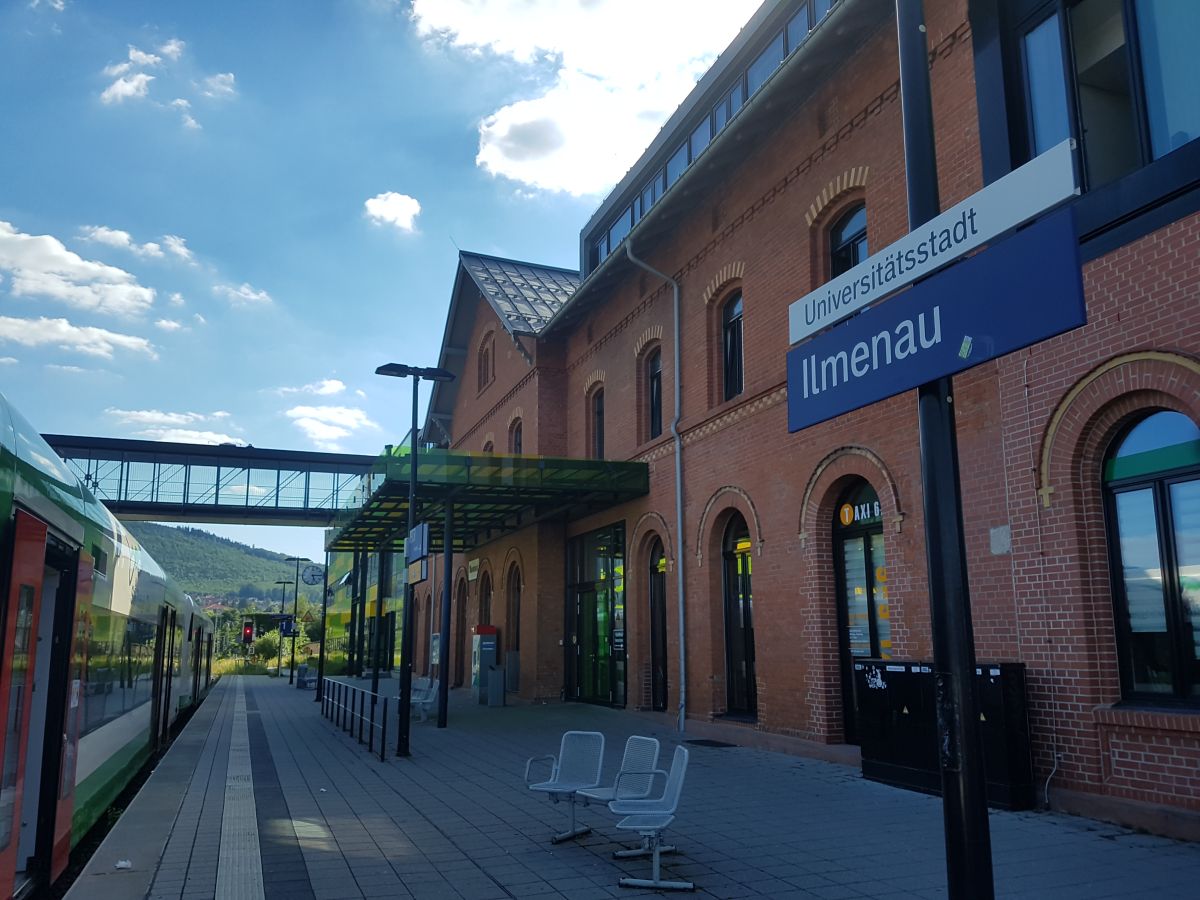 train station with sign university city Ilmenau: on the left side a train, on the right side a building